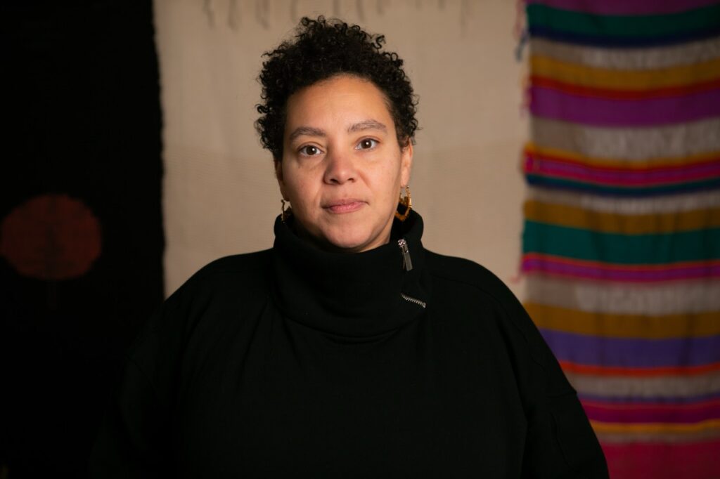 Alisha B. Wormsley stands in front of three of her textile art pieces.