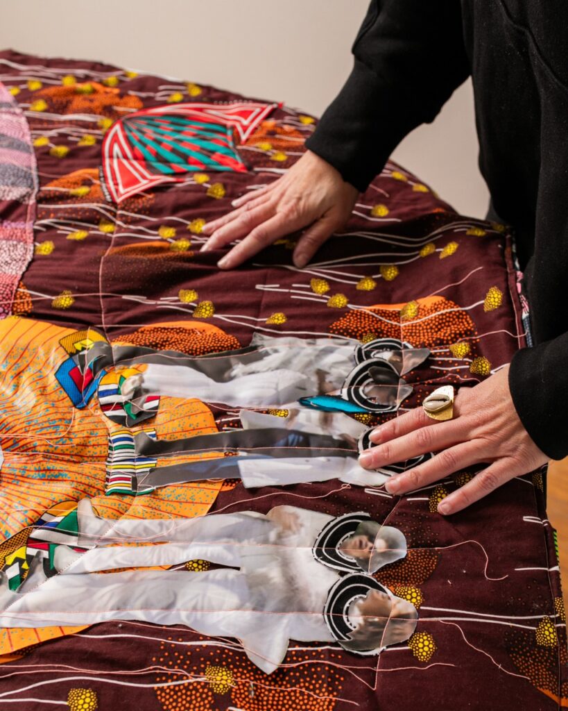 A woman lays her hands on a large quilt with details throughout.