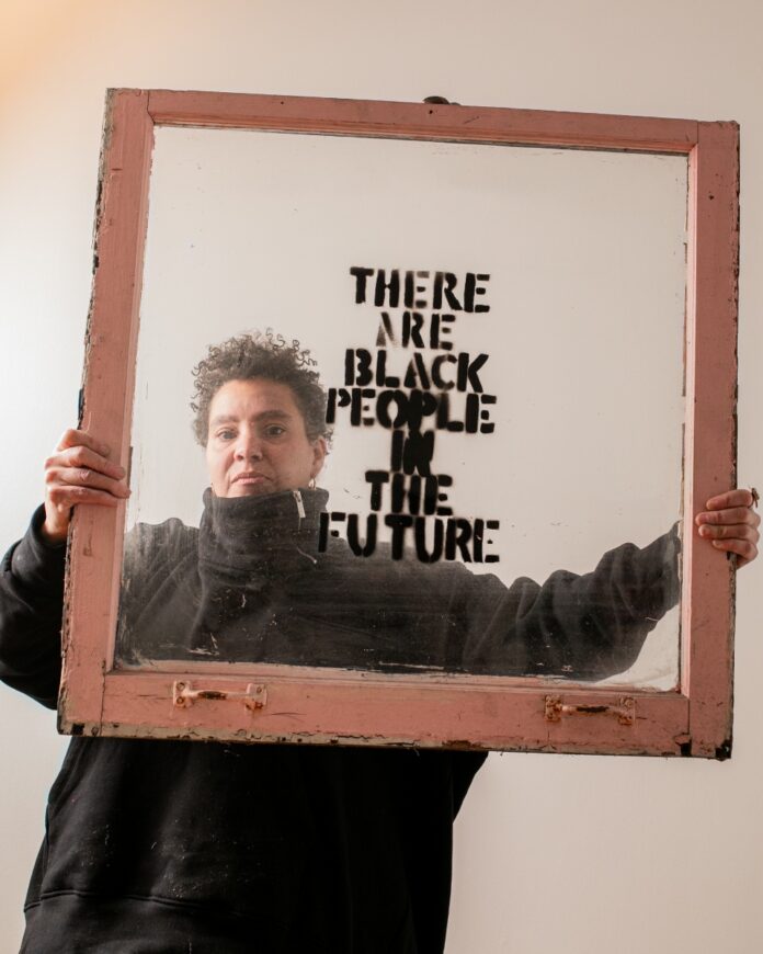 Pittsburgh artist Alisha B. Wormsley holding an antique brown window frame featuring her iconic "There Are Black People In The Future" text, a key piece of her socially engaged art practice.