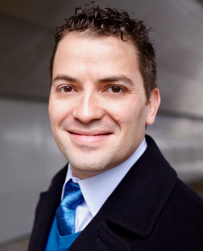 Andrés Franco stands in a black suit jacket with a blue tie.