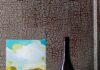 Nicole Renee Ryan’s Paintings Offer an Analog Antidote at Shoppe B in Lawrenceville A small painting of a bright landscape by Nicole Renee Ryan sits on a stack of books beside a bottle of Vara wine.