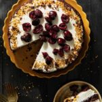 A Black Forest Cake in a pan with white frosting and brandied cherries on top.
