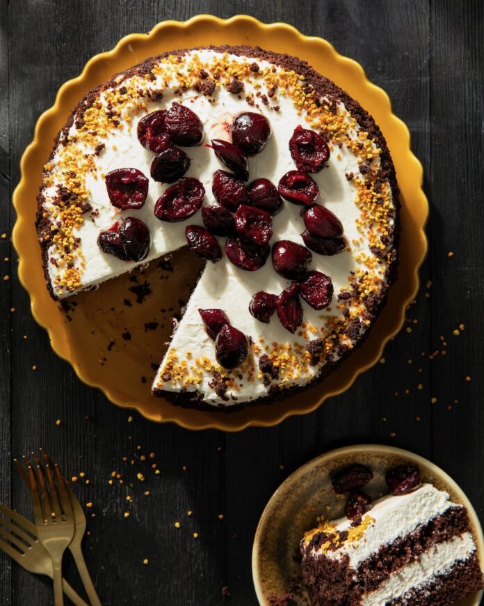 A Black Forest Cake in a pan with white frosting and brandied cherries on top.