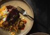 Black Pepper Crusted Short Ribs Two plates with Black Pepper Crusted Short Ribs, a corn hash, and grilled peppers in yellow and green.