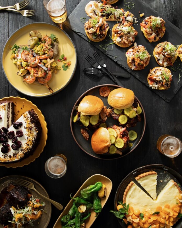 Various plates of black and gold foods for the Steelers like BBQ pork sandwiches, tarts, cakes, grilled grimp, and tostadas.