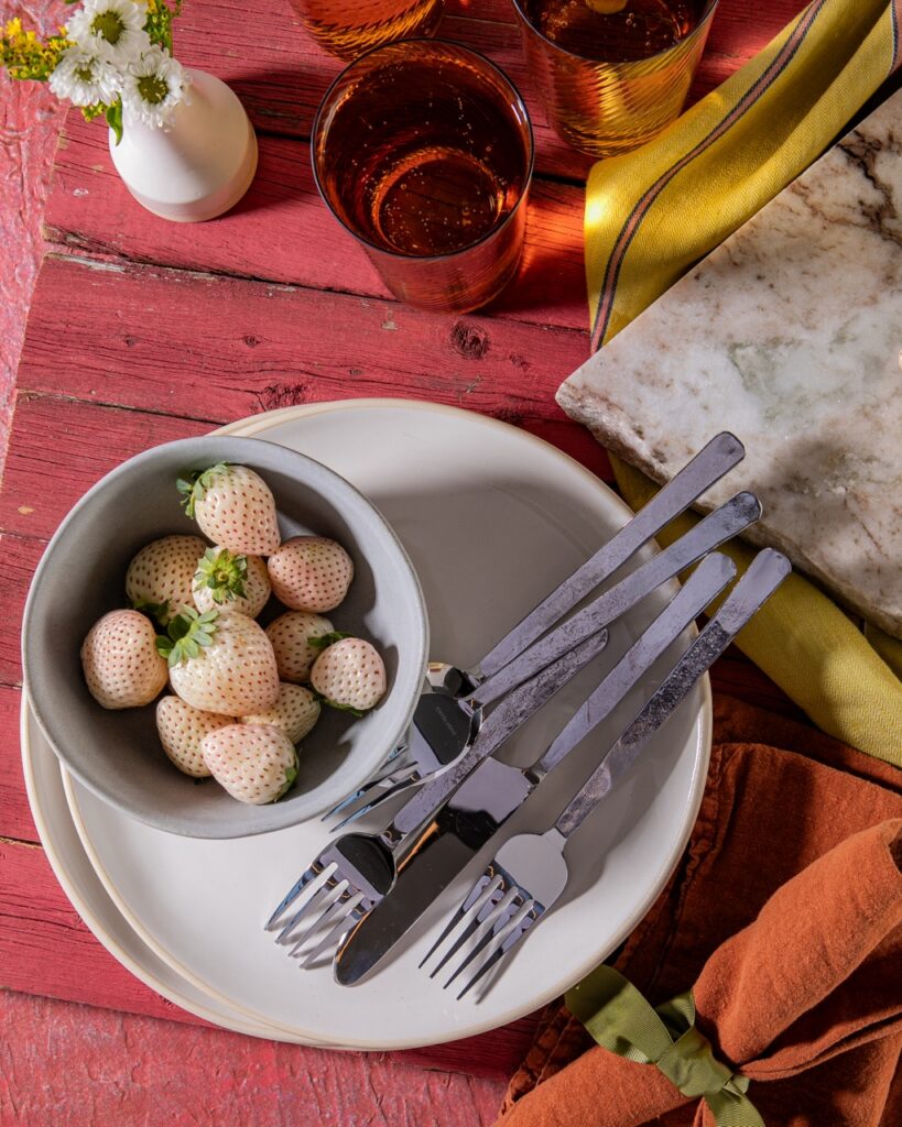 A white plate sits on a red wood table with a bowl of white strawberries on top of the plates.