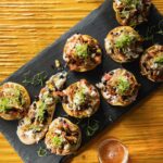 Small Blackened Cajun Chicken Tostadas sit on a black rectangular tray on top of a wood table.