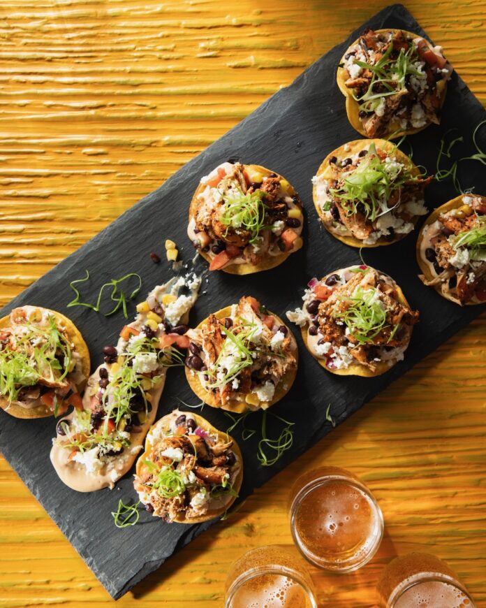 Small Blackened Cajun Chicken Tostadas sit on a black rectangular tray on top of a wood table.