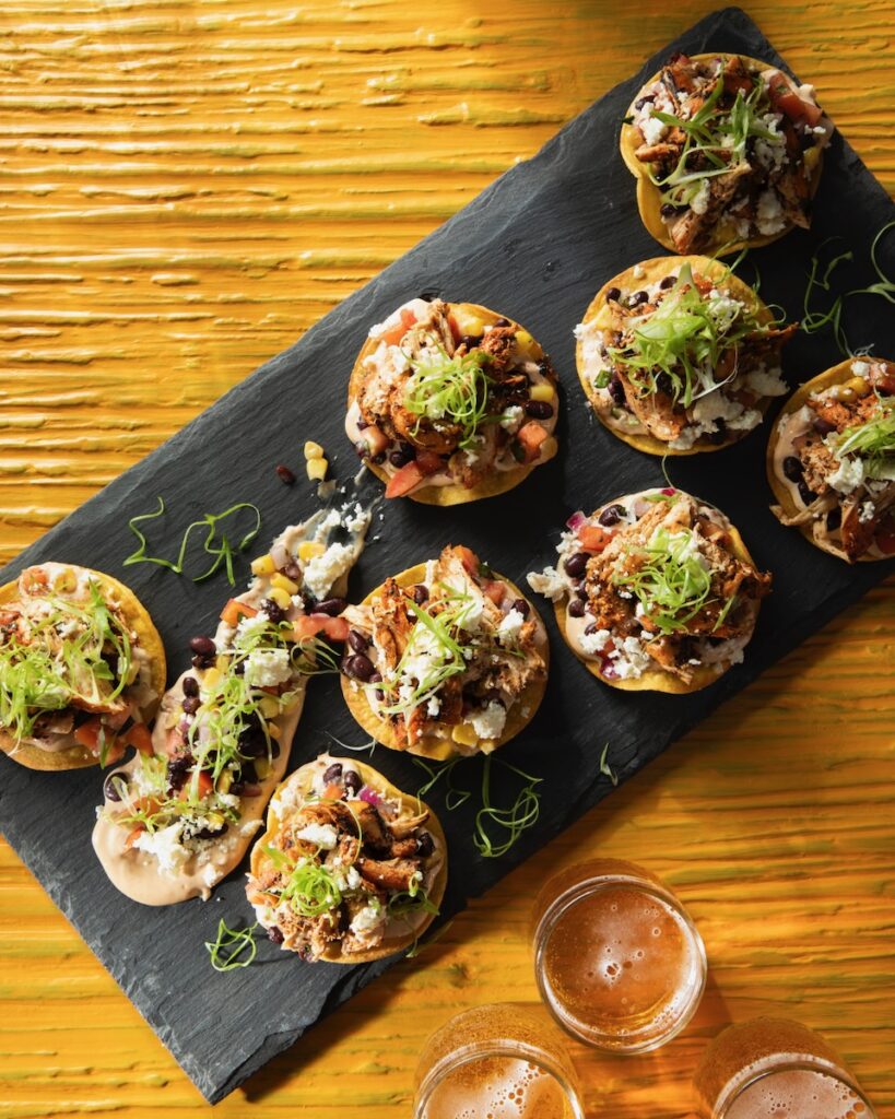 Small Blackened Cajun Chicken Tostadas sit on a black rectangular tray on top of a wood table.