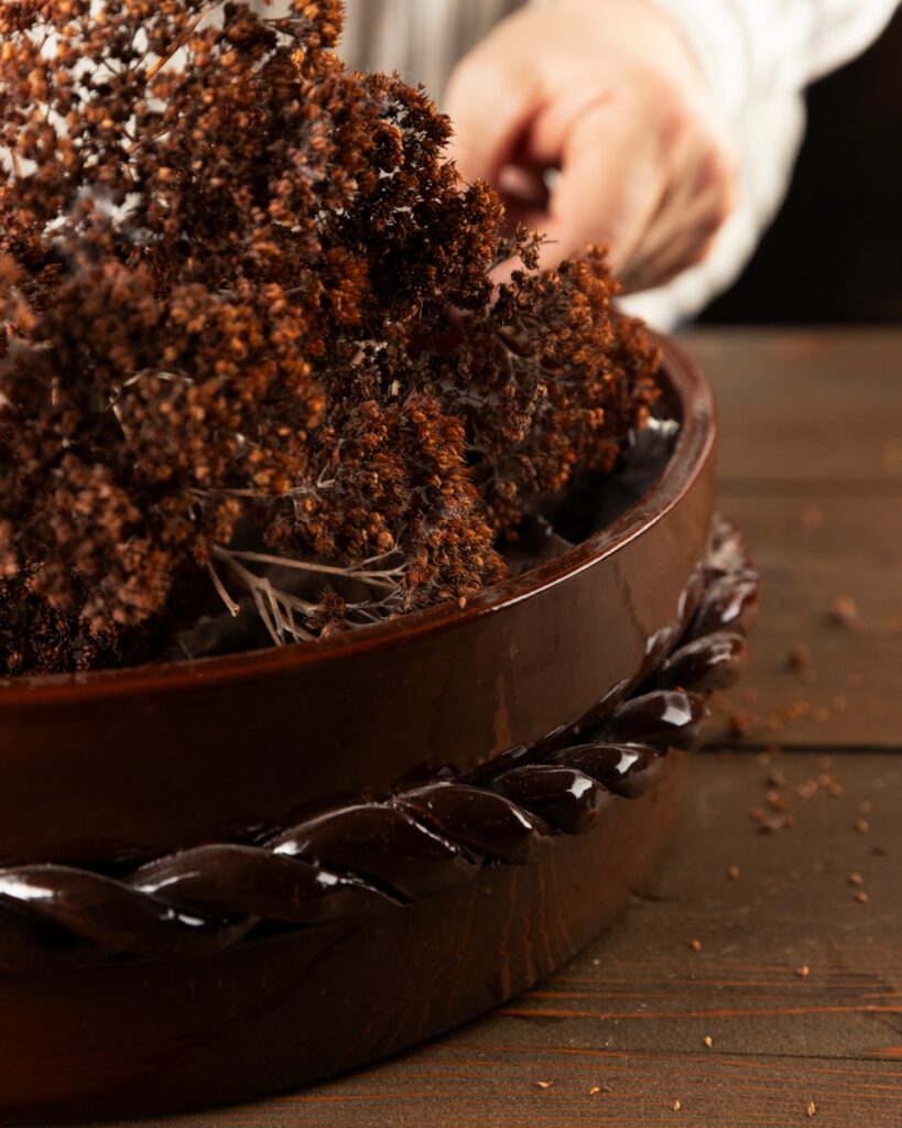 A deep chocolate brown glazed ceramic bowl from Weisshouse, featuring a distinctive twisted rope-style trim around the exterior and filled with dried botanicals.