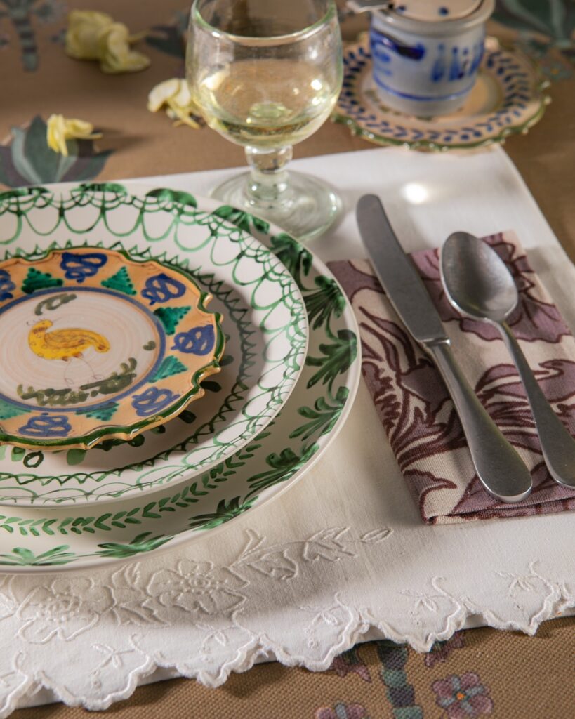 A stack of three green pattern plates sits beside a pattern napkin with a spoon and knife on top of it.