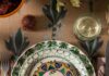 Cara George of Otea Tells a Family Story in Textiles and Table Settings Three green pattern plates stacked on top of a brown table cloth setting with silverware on each side.