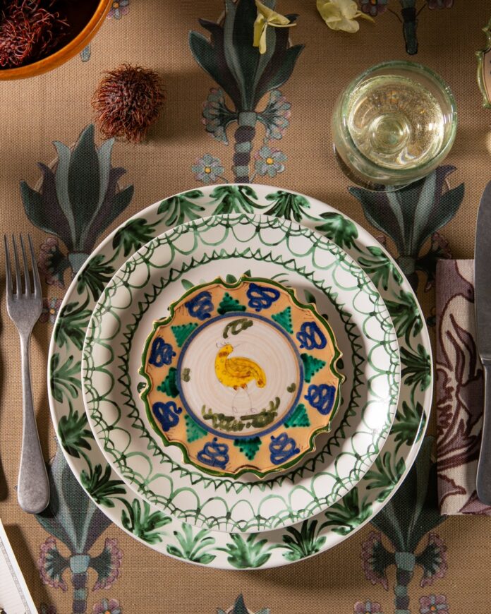 Three green pattern plates stacked on top of a brown table cloth setting with silverware on each side.
