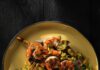 Char Grilled Shrimp Skewers A yellow plate of char grilled shrimp skewers with blue corn grits and golden beet salad under it and slices of charred limes on the sides.