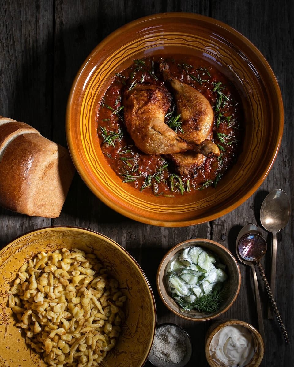 Chicken Paprikash served in a bowl along with bread and side dishes