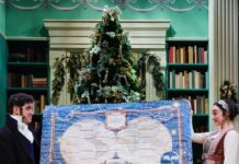 City Theatre Announces a Bold, Collaborative 2026-27 Season A man and woman in costume hold up a quilt on stage in front of a Christmas Tree.