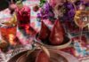 Colleen Simonds’ Table Setting Encourages Color Drenching A purple pear on a small bowl on top of bigger mauve plate all on a pattern table cloth of blue and pink.