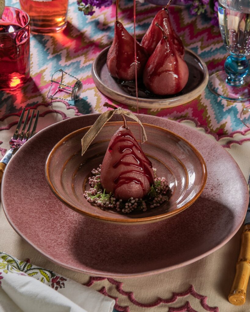 A drizzled peach sits in a mauve bowl under a similar color plate and with a small plate of three pears sitting in the background.
