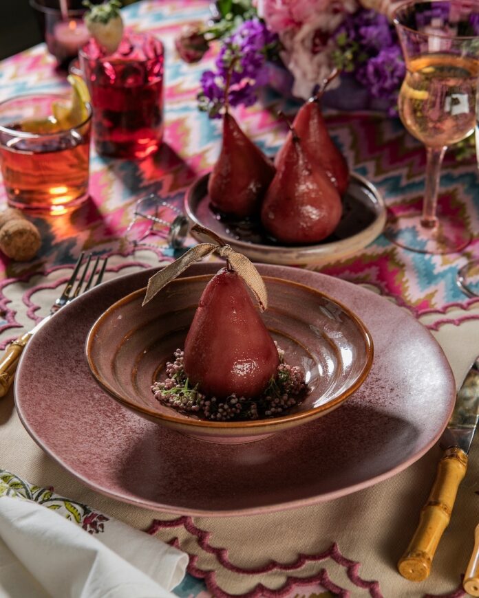 A purple pear on a small bowl on top of bigger mauve plate all on a pattern table cloth of blue and pink.
