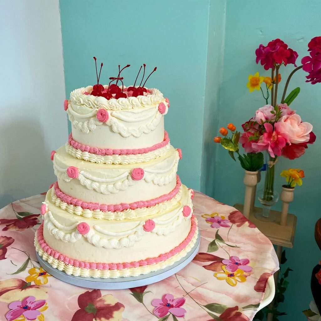 A layered cake with pink and white icing and cherries all over the top.