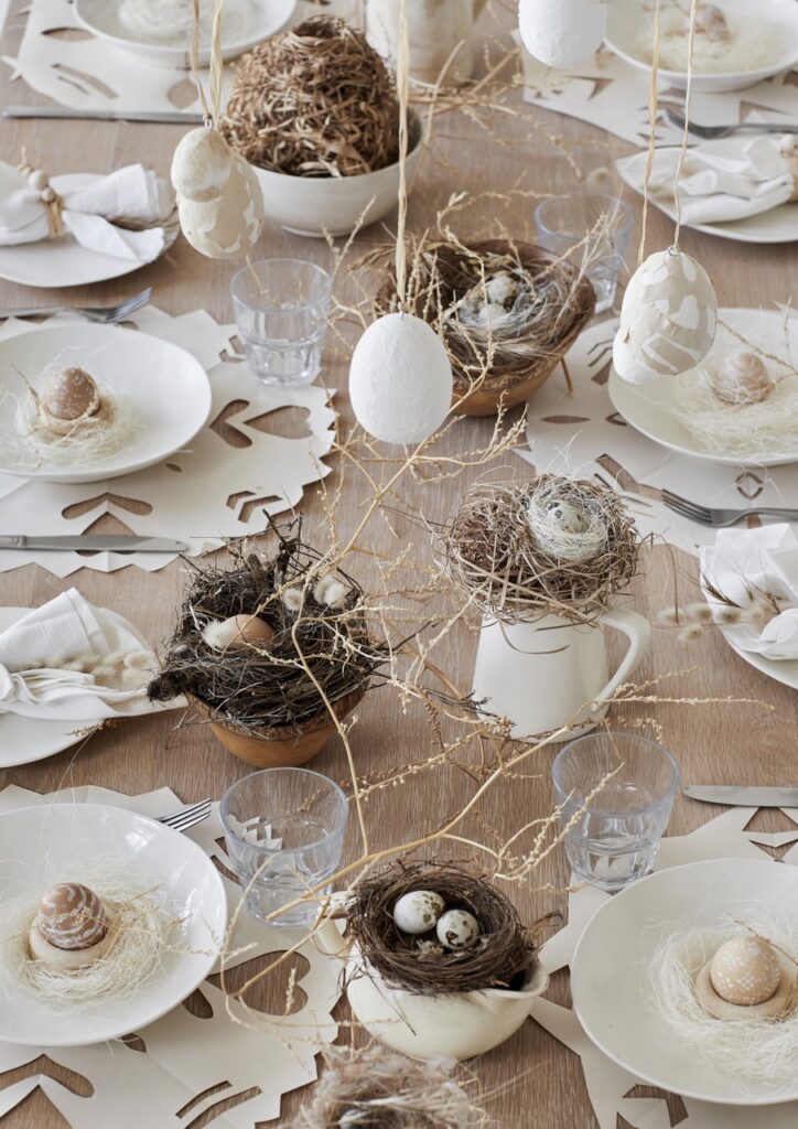 Various white plates featuring eggs sit amongst a table of nest and egg Easter DIY decor.