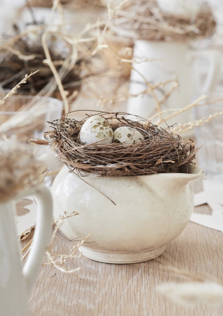 A birds nest with eggs in it sits in a large cream colored pot.
