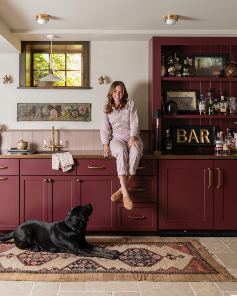 Dana Mackey sits on a burgundy countertop with her black lab laying below her.