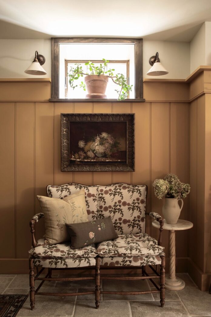 Below a basement window sits a loveseat and framed flower painting.