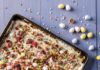 Easter Crack (Saltine Cracker Toffee) A tray of Easter Crack with half mini chocolate eggs everywhere, eggs above the tray and flowers below it.
