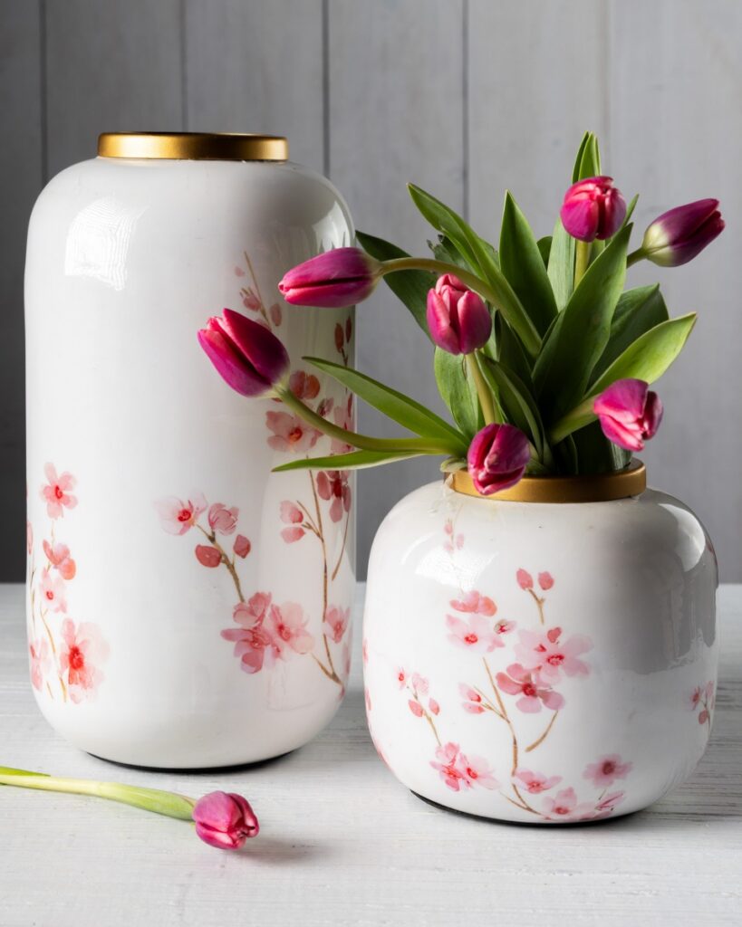 Two white porcelain Splurge vases with gold rims and hand-painted pink cherry blossom designs, one tall and one short, holding fresh pink tulips.