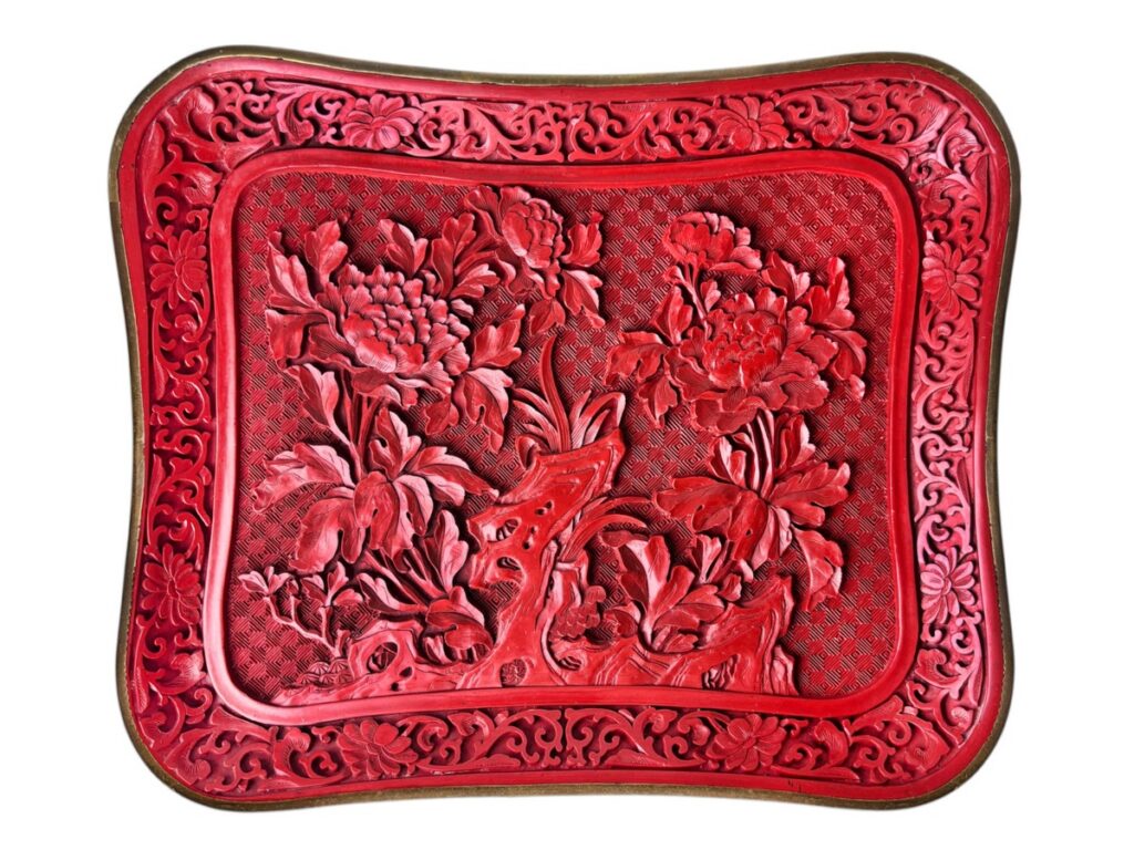 An antique Chinese cinnabar lacquer tray from Asian Influences featuring a deeply carved central peony flower design, floral banding at the rim, and a brass edge.