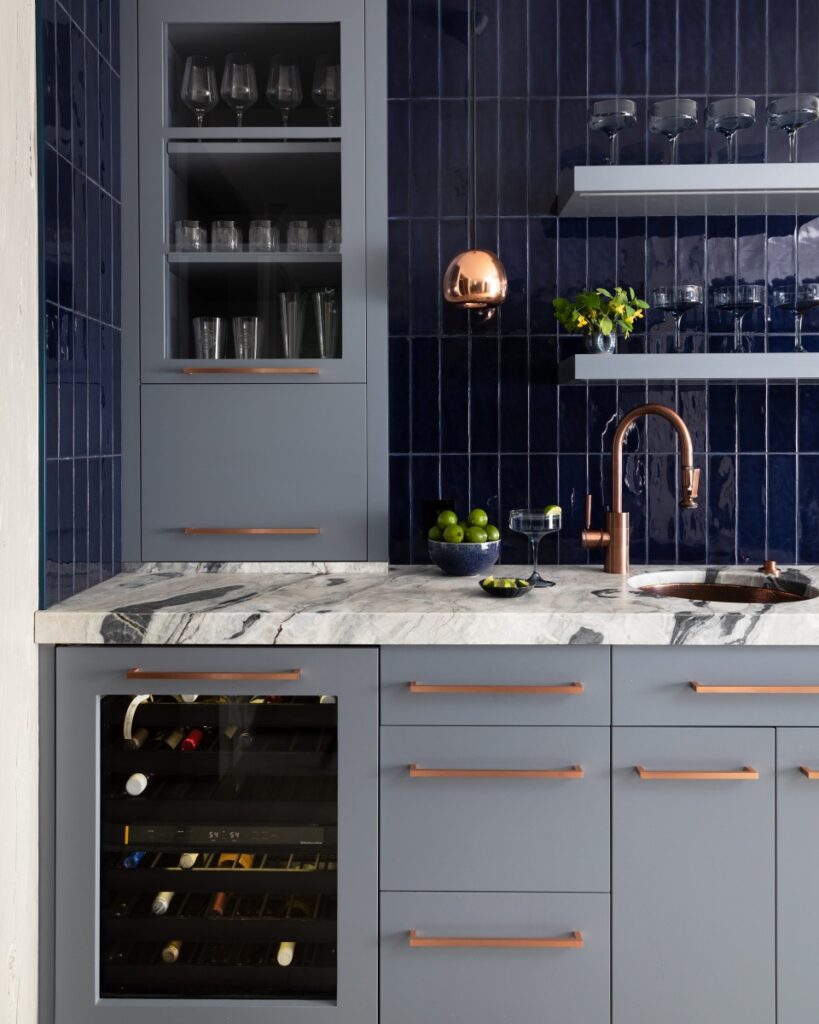 A contemporary wet bar in a Fox Chapel farmhouse featuring deep blue subway tile, grey cabinetry with copper hardware, a copper sink, and a built-in wine cooler.