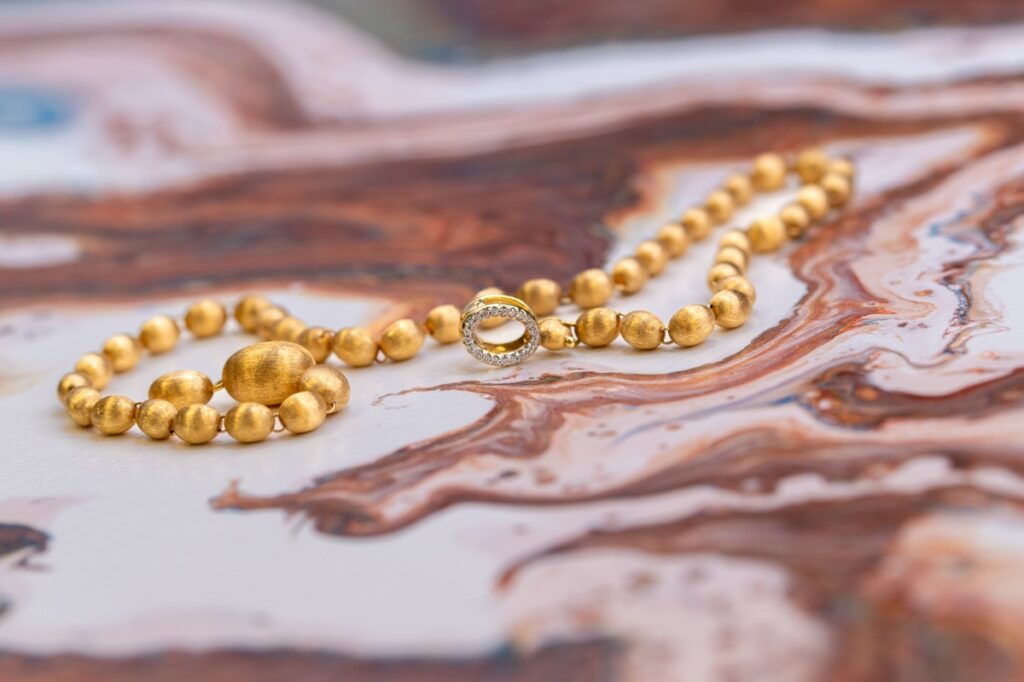 Nanis Ivy necklace in 18k yellow gold featuring hand-engraved millerighe beads and a diamond clasp, available at Henne Jewelers.