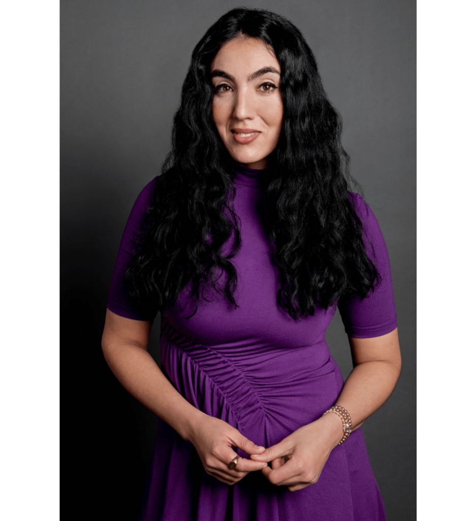 A woman in purple with long dark culry hair.