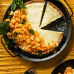 A circle pan holds a vanilla custard tart with sliced gold berries all along one side.