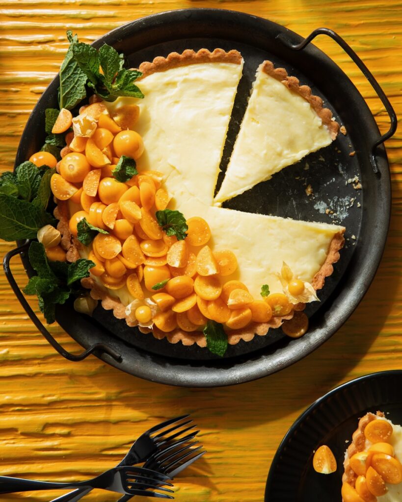 A circle pan holds a vanilla custard tart with sliced gold berries all along one side.