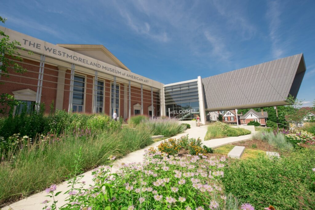 The modern exterior of the Westmoreland Museum of American Art in Greensburg, featuring a sleek cantilevered glass wing and a paved courtyard at dusk.