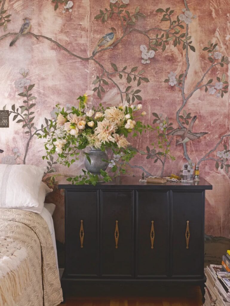 A bedroom wall covered in de Gournay's Rose Antiqued Badminton chinoiserie wallcovering, featuring hand-painted birds and flowers on tarnished silver-gilded paper.