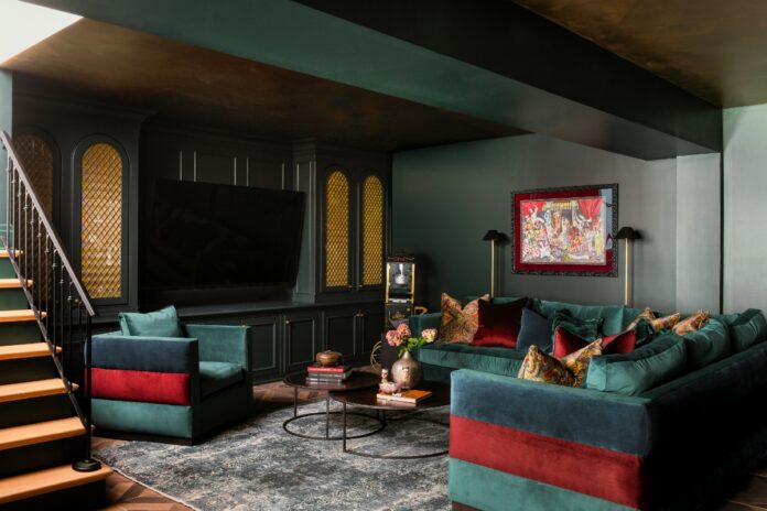 A luxurious basement lounge designed by Seashal Belldina featuring deep green color-washed walls, a gold ceiling, jewel-tone velvet seating, and a modern bar.