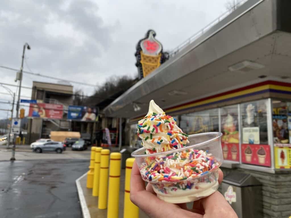 Vanilla soft serve in a clear cup with rainbow sprinkles.
