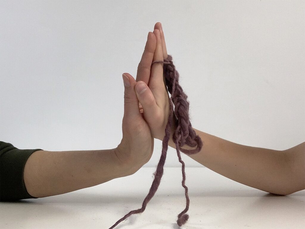 Two people touch palms of hands with rope wrapped around them.