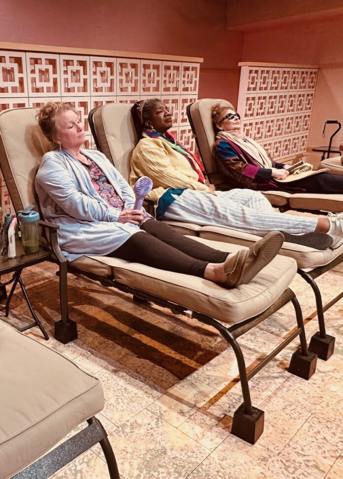 Three women lay on beach lounge chairs, in clothing.
