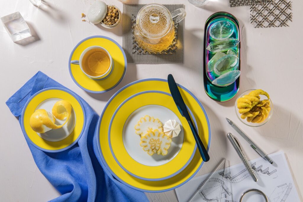 A stack of yellow and blue plates sits on a table with blue napkins and other yellow embellishments like a yellow saucer.