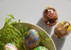 5 Ways to Dye Easter Eggs A bowl holds Pysanky designed Ukrainian Easter eggs with green easter grass underneath them and some loose on the table.