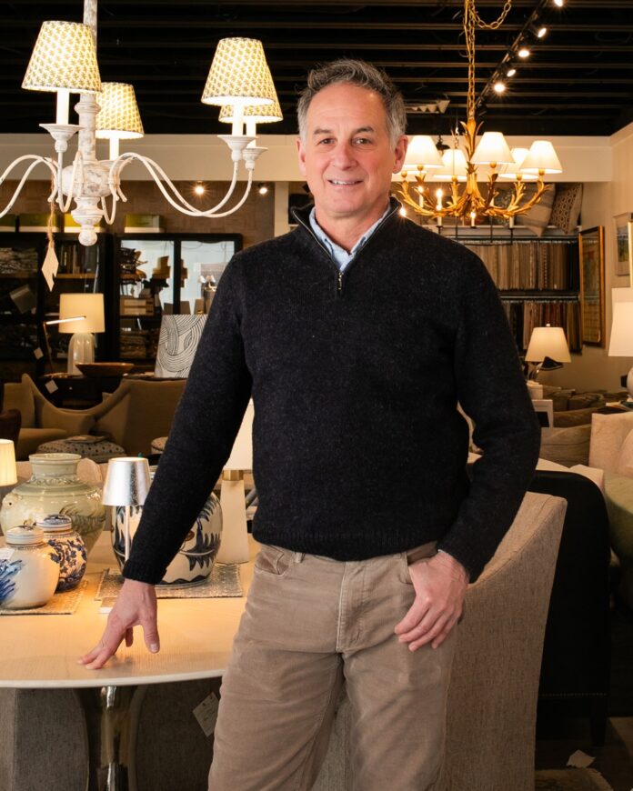 Jay Miller stands at a table in khakis and a black sweater.