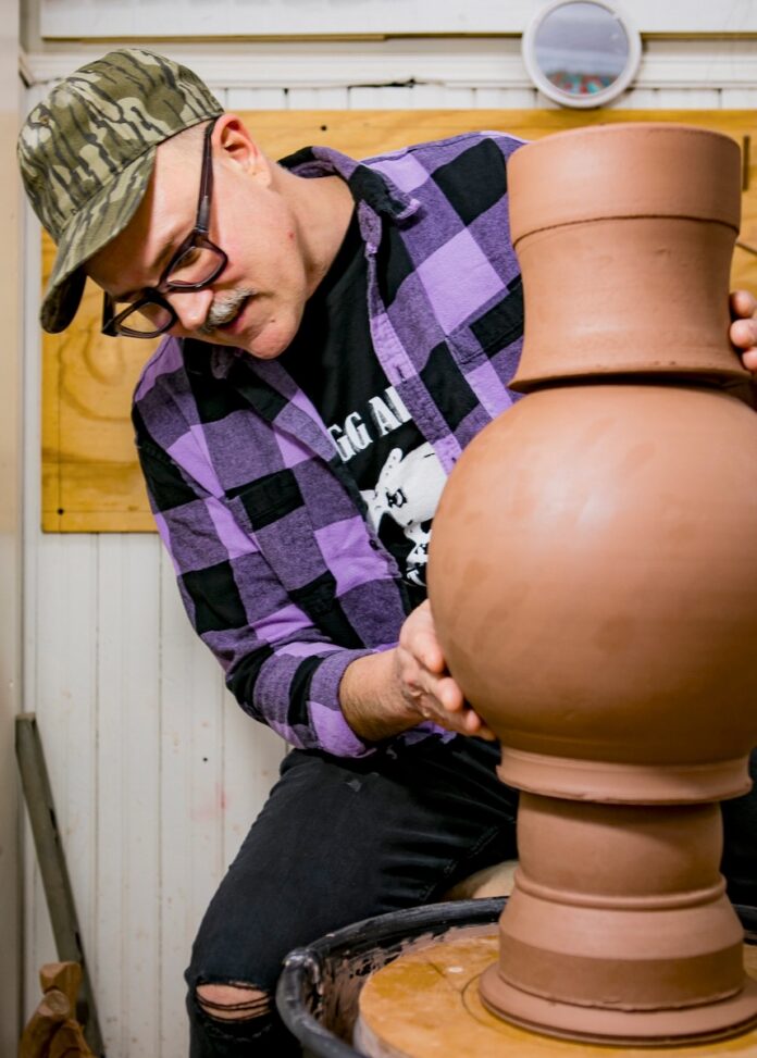 A man sculpts a piece of clay into a vase on a pottery wheel.