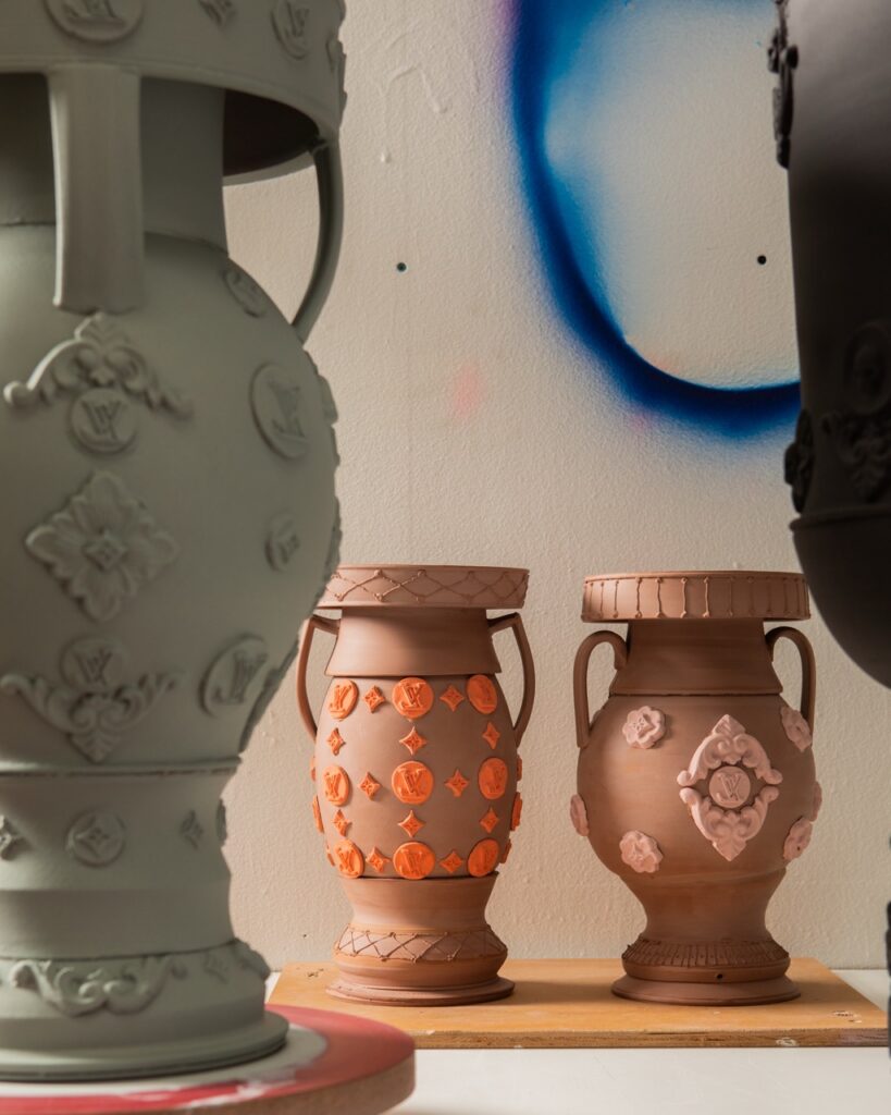 A grey detailed vase sits in front of two other clay vases with details.