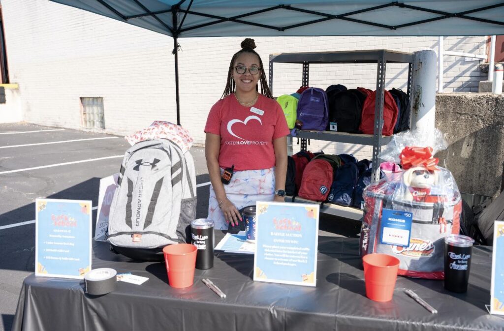 A woman stands behind a booth for Foster Love Project with a red shirt on.
