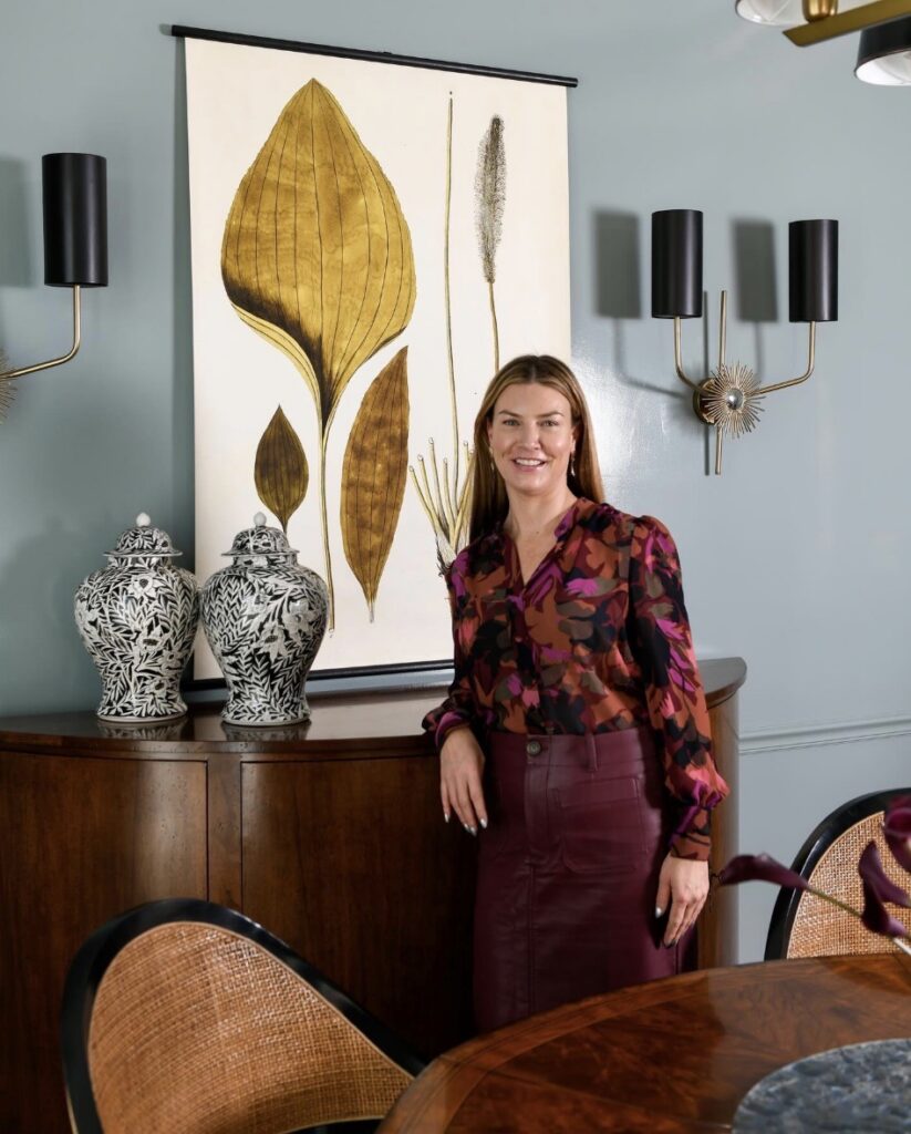 A woman in red learns against a cabinet and painting.