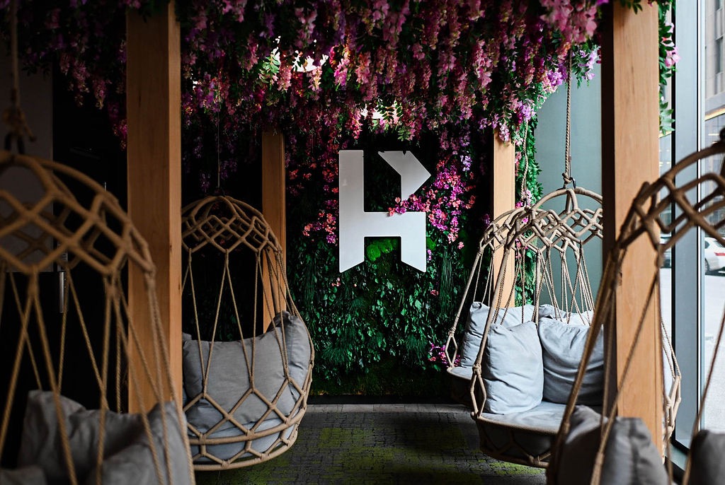 The inside of Ritual House with an R on a floral wall and swings surrounding it.
